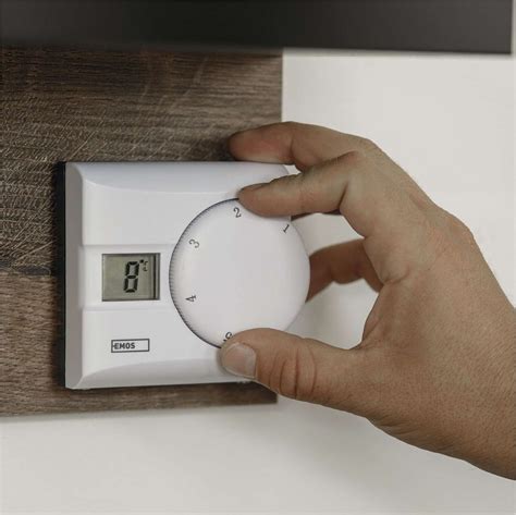 Ilustračná fotografia moderného bezdrôtového izbového termostatu s mobilným telefónom v ruke