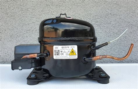 Detailný pohľad na kompresor chladničky s vyznačenými trubicami a pripojeniami.